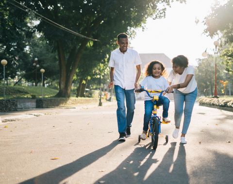 Deux parents apprennent le vélo à leur enfant dans un parc au soleil