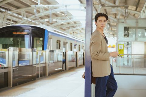Un homme attend son train sur un quai de gare, téléphone à la main